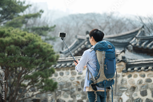 A young man who travels to Korea is taking pictures using his smartphone.