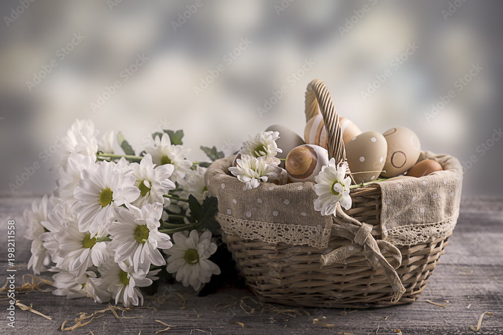 Easter eggs beige in a basket on a table. White flowers nearby