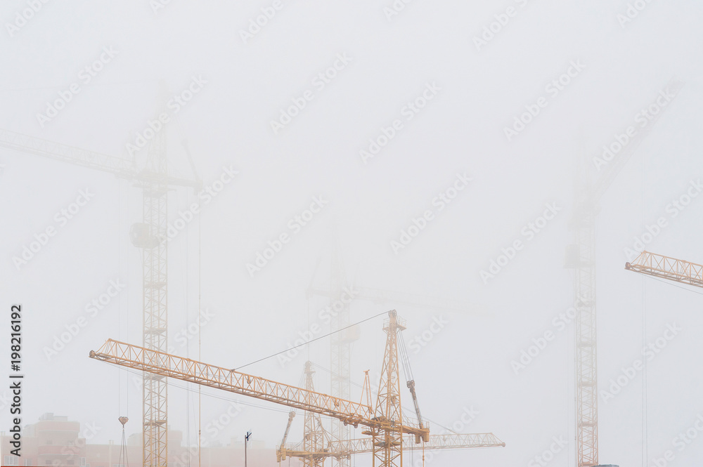 yellow tower cranes in misty haze