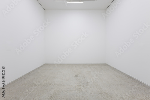 A view of a white painted interior of an empty room or an art gallery with a fluorescent lighting and concrete floors