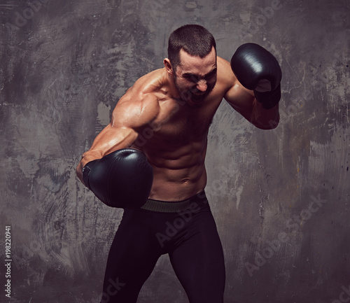 A brutal muscular boxer with boxing gloves working on punching technique. © Fxquadro