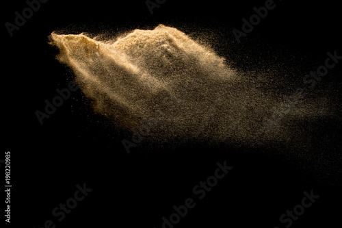 Golden sand explosion isolated on black background. Abstract sand cloud. Golden colored sand splash against dark background. Yellow sand fly wave in the air.