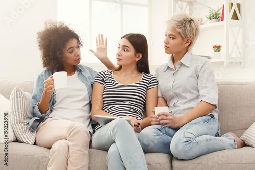 Three female friends using tablet and drinking coffee