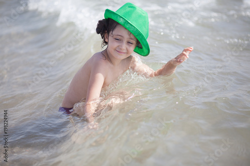 Little girl in a green hat swims and plays in the sea photo