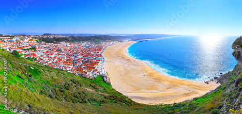 Wonderful romantic afternoon panoramic landscape coastline of Atlantic ocean. View Nazare beach riviera (Praia da Nazare) with cityscape of Nazare town in low season at sunny weather. Portugal.