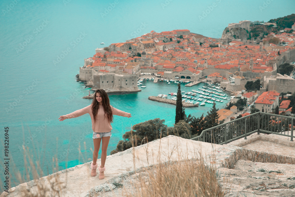 Obraz premium Brunette Girl tourist visiting mountain viewpoint sightseeing in Dubrovnik, Croatia. Woman traveller in front on famous travel destination. Free brunette enjoying vacation.