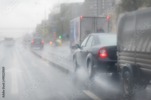 Black car with a cargo trailer in the rain on the asphalt wet road. Gray Clouds on the sky .