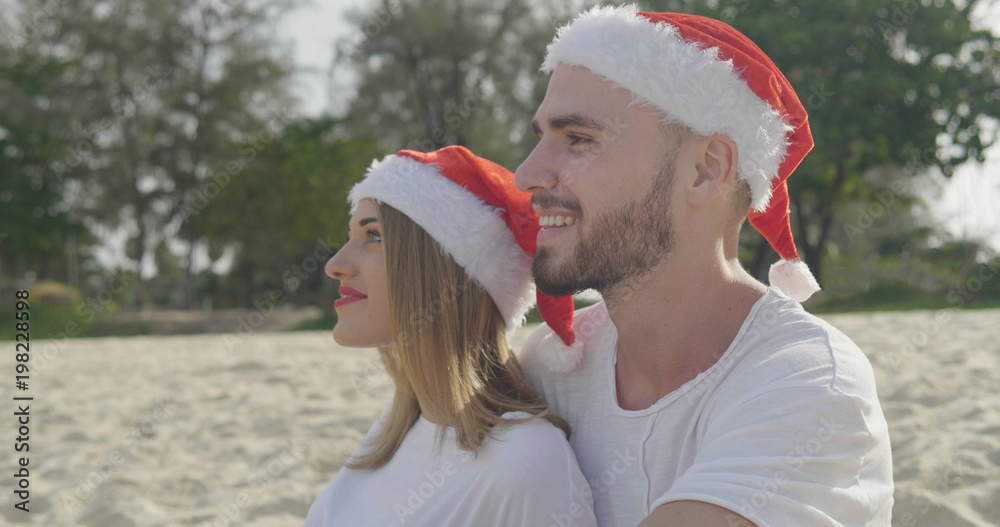 Obraz premium Christmas beautiful beach couple wearing Santa hat in summer sun in love on travel holidays on tropical travel destination during winter holidays
