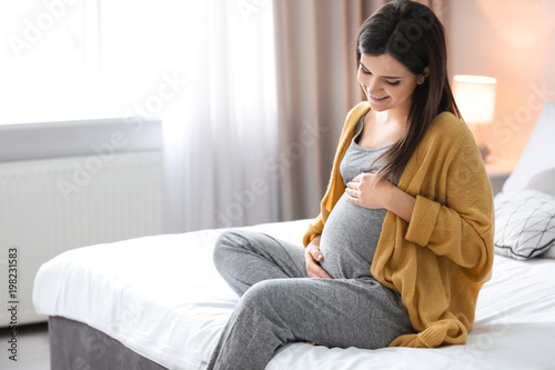 Young pregnant woman sitting on bed at home