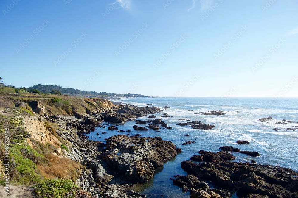 Beautiful scenic coastal view in California (USA): Untouched nature of the pacific ocean with limestone rock cliffs and crashing waves with a clear blue summer sky create the perfect picturesque place