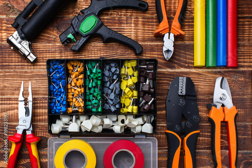 background of professional electrician tools: cable lugs in the organizer box, insulating tape, earplugs, cutters, tips, burnerpuller insulation, on a wooden board