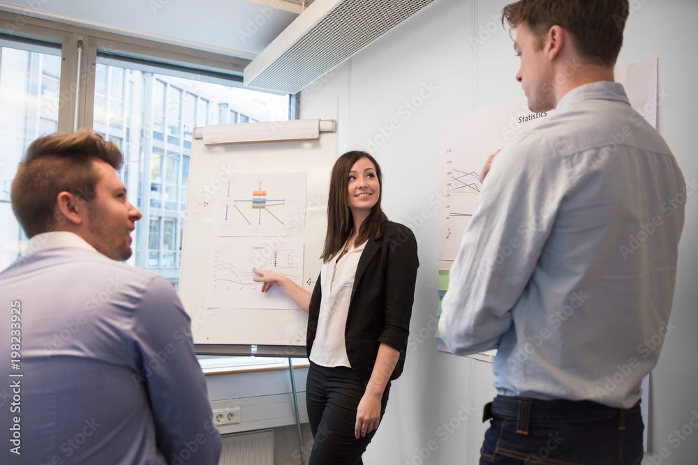 Smiling Female Professional Explaining Chart To Colleagues Smiling Female Professional Explaining Chart To Colleagues