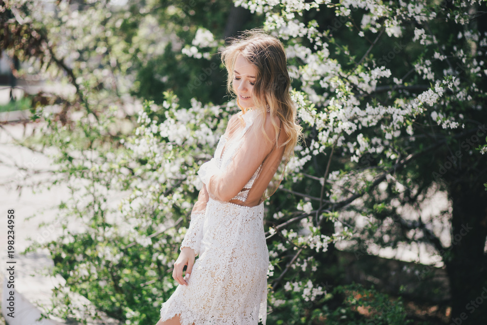 Beautiful young woman in a white romantic dress posing near blooming tree Beautiful young woman in a white romantic dress posing near blooming tree