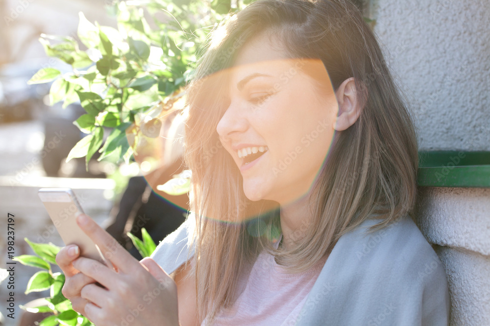 Smiling happy young woman with smart phone. Sunny day, backlight Smiling happy young woman with smart phone. Sunny day, backlight