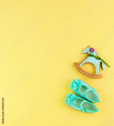 Baby girl shoes and toy horse cookie on yellow background with copy space