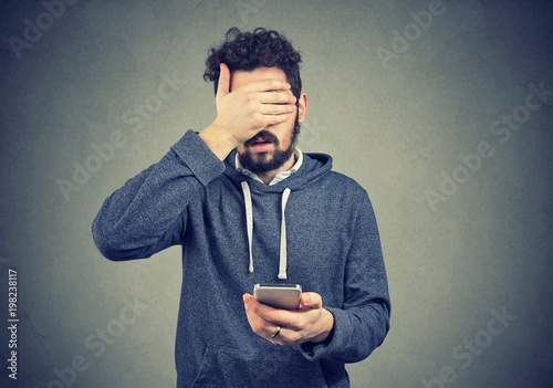 Sad regretful young man with mobile phone