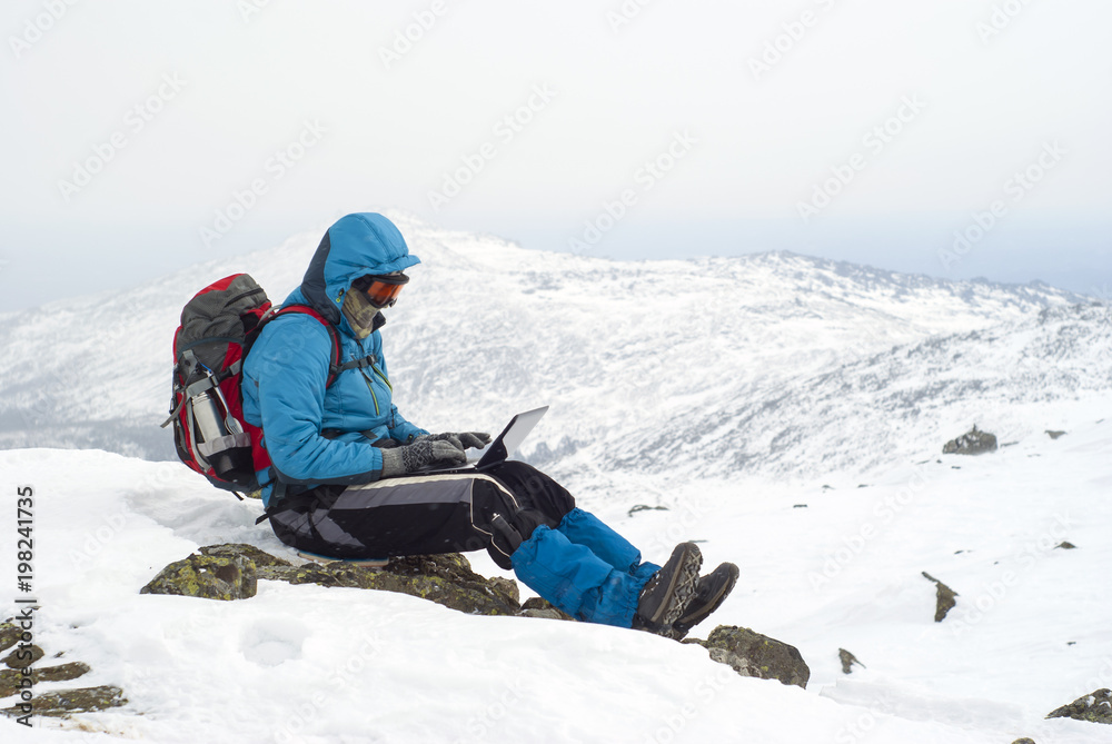 traveller working with a laptop in winter on top of a mountain during the snowstorm traveller working with a laptop in winter on top of a mountain during the snowstorm