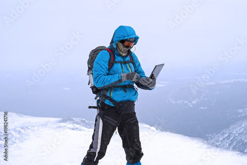 climber working with a laptop in winter on top of a mountain in extreme conditions