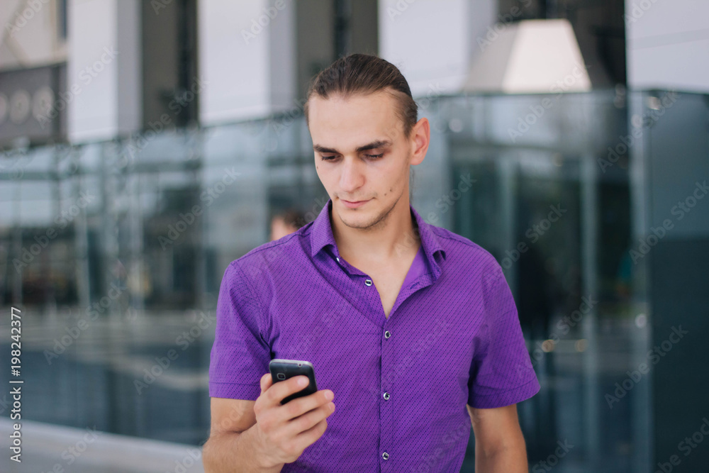 A handsome, young guy in a purple shirt is talking on the phone. Model of a man in a mall with a mobile phone in his hand