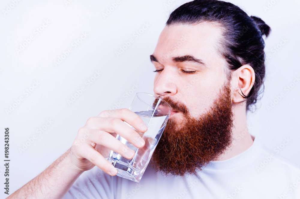 Hipster drinking clean healthy water, refreshing. Man with long beard hold water glass on grey background. Hangover and thirst. Health and dieting. Life source and healthcare. Hipster drinking clean healthy water, refreshing. Man with long beard hold water glass on grey background. Hangover and thirst. Health and dieting. Life source and healthcare.
