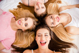 Top view self portrait of sexy, charming, funny, foolish, blonde, brunette, pretty, cheerful girls lying head to head on bed blinking with one eye, looking at camera, enjoying meeting indoor
