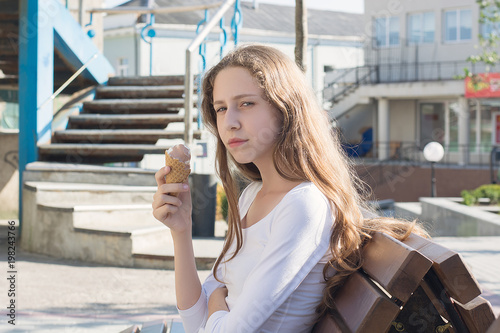 Young beautiful girl with ice cream sitting on a bench in summer.