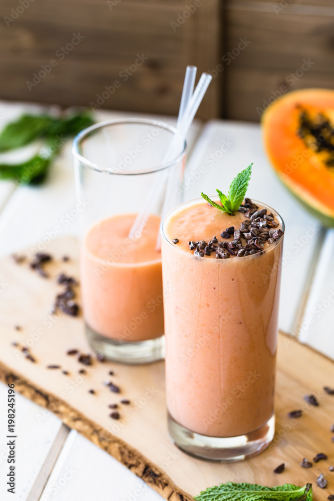 Vegan Papaya Smoothie Banana Milkshake Cacao Nibs and Mint on top on White Wooden Background Vegan Papaya Smoothie Banana Milkshake Cacao Nibs and Mint on top on White Wooden Background
