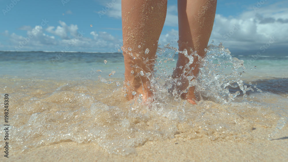 CLOSE UP: Woman stands in hot white sand and lets small waves cool off her feet.