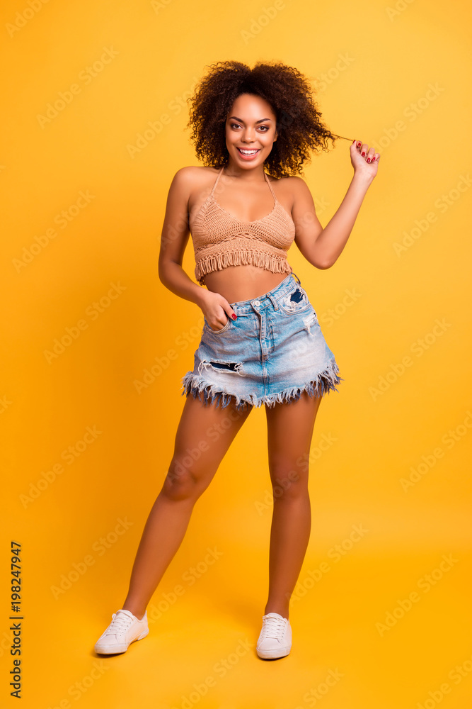 Vertical vyll-size full-length portrait of charming tempting beautiful lovely with afro curly hair wearing casual summer clothes woman, she is holding hand in pocket, isolated on yellow background Vertical vyll-size full-length portrait of charming tempting beautiful lovely with afro curly hair wearing casual summer clothes woman, she is holding hand in pocket, isolated on yellow background