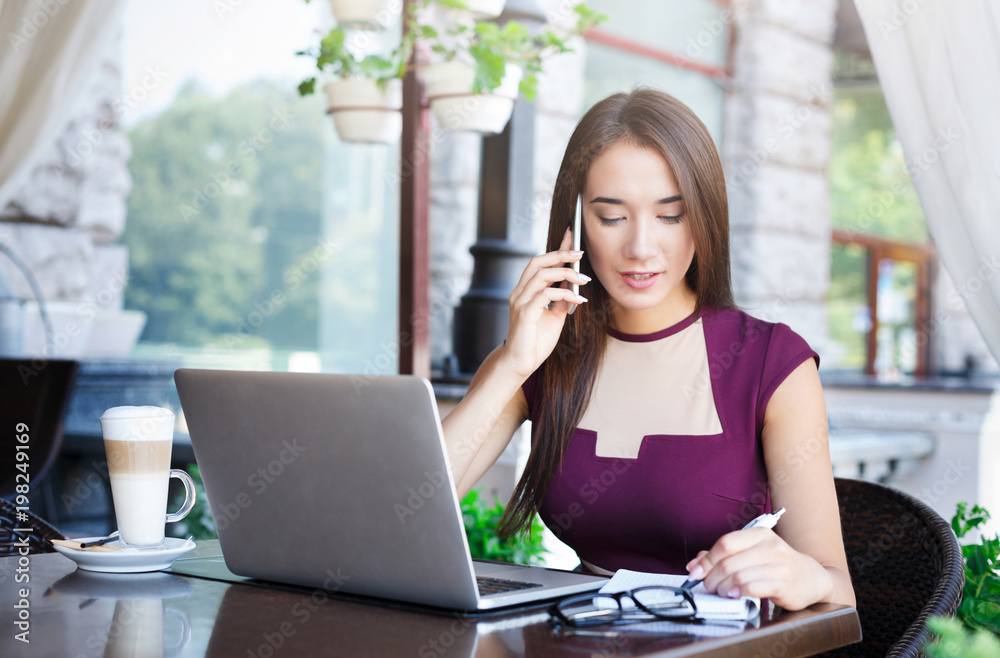 Young businesswoman talking on smartphone and making notes Young businesswoman talking on smartphone and making notes