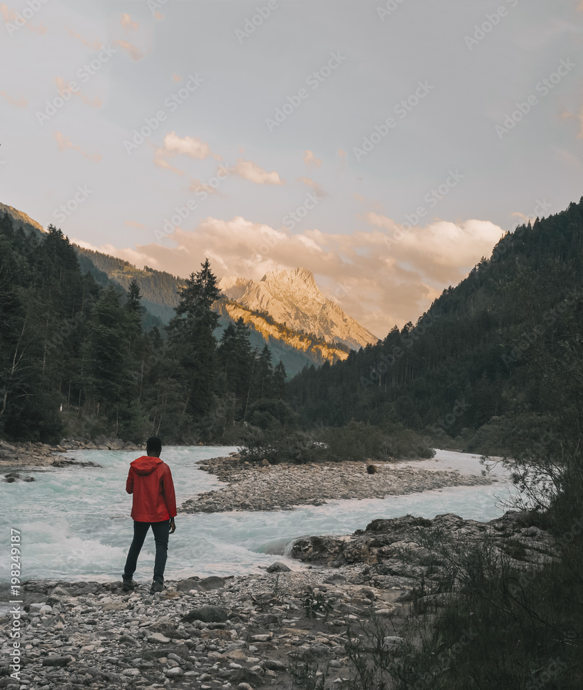 Hiker looking at view while standing by river against mountains Hiker looking at view while standing by river against mountains