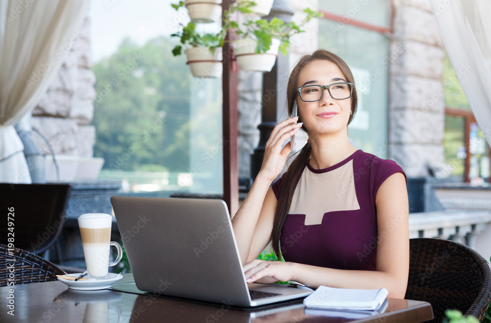 Fototapeta premium Young businesswoman working on laptop and talking on phone