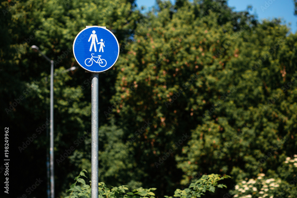 pedestrian bicycle zone in blue circle on background of green trees in park. city street sign concept. sign with person and child and bicycle in white and blue circle.