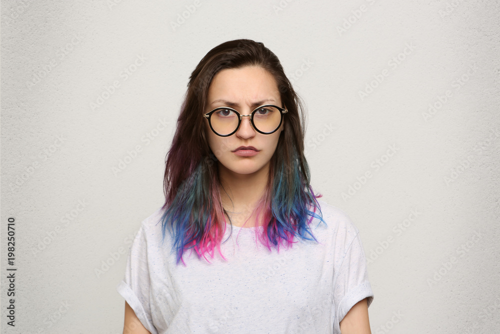 What? Indoor shot of young girl with dyed colorful hair wears white casual t-shirt and round spectacles feels puzzle isolated over white wall What? Indoor shot of young girl with dyed colorful hair wears white casual t-shirt and round spectacles feels puzzle isolated over white wall