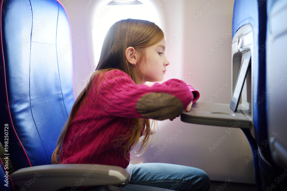 Adorable little child traveling by an airplane. Girl sitting by aircraft window and reading her ebook during the flight.