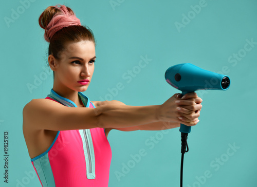 Happy young brunette woman pointing hair dryer on blue mint 