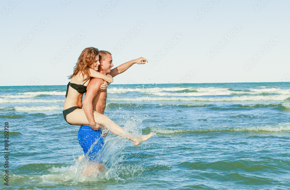 happy couple play in the sea. sexy girl piggybacking in the ocean. on man and water splashing.