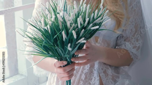 Unrecognizable young slim sexy blond girl in lingerie and boudoir sitting in windowsill and lookingin at artificial flowers in her hands. photo