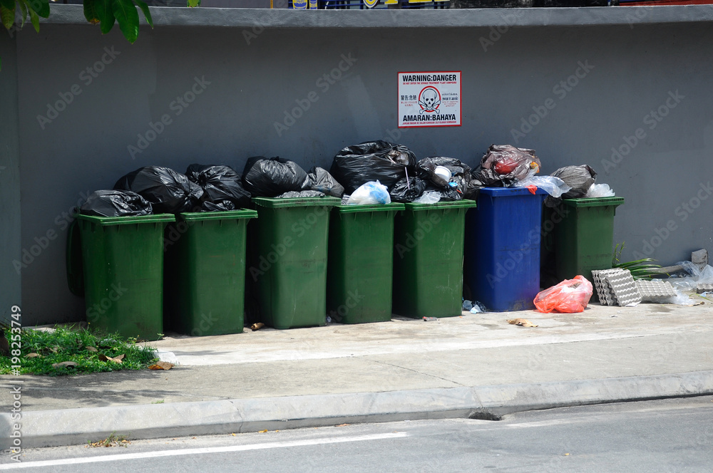 Rubbish bin and pile of overload trash in black plastic bag. Stock