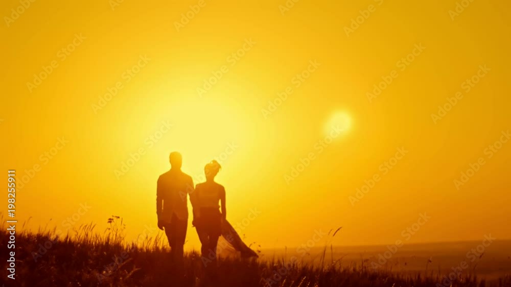 Loving couple - young man and beautiful girl walking at sunset meadow - silhouette Loving couple - young man and beautiful girl walking at sunset meadow - silhouette