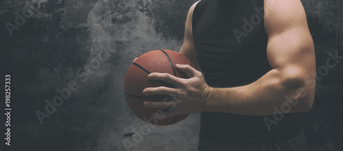 Male basketball player with a ball over dark background. Fit young man in sportswear holding basketball.