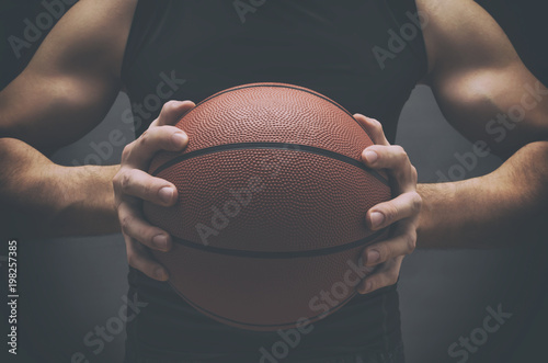 Male basketball player with a ball over dark background. Fit young man in sportswear holding basketball. © NatasaAdzic