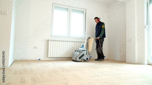 Sanding hardwood floor with the grinding machine. Repair in the apartment. Carpenter doing parquet wood floor polishing maintenance work by grinding machine