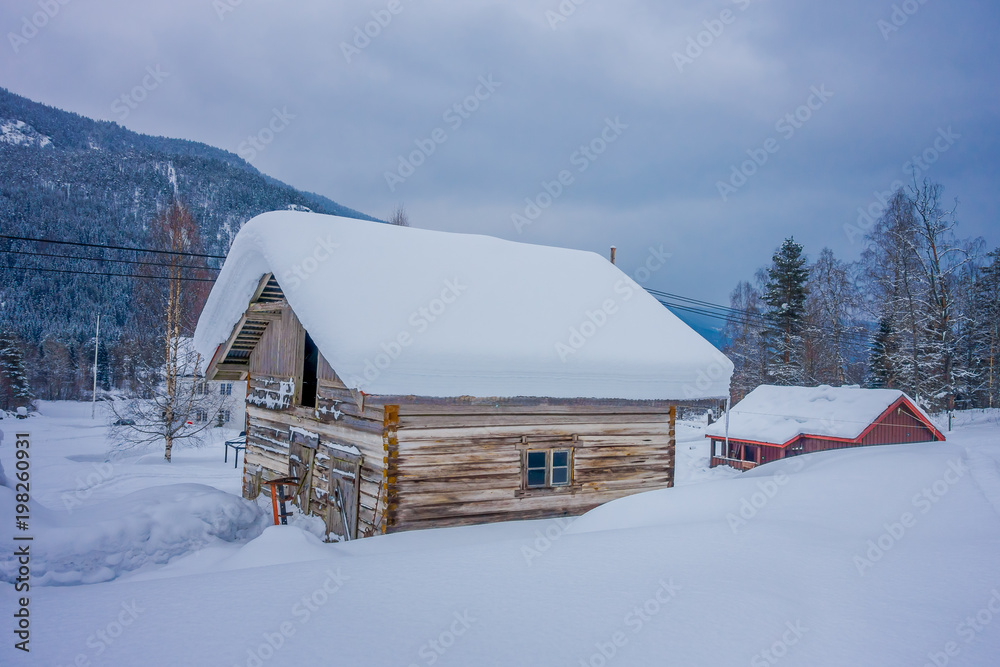 View of traditional wooden houses covered with snow in stunning nature background and huge mountain behind in Norway