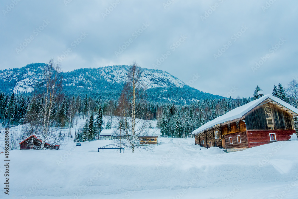 View of traditional wooden houses covered with snow in stunning nature background and huge mountain behind in Norway