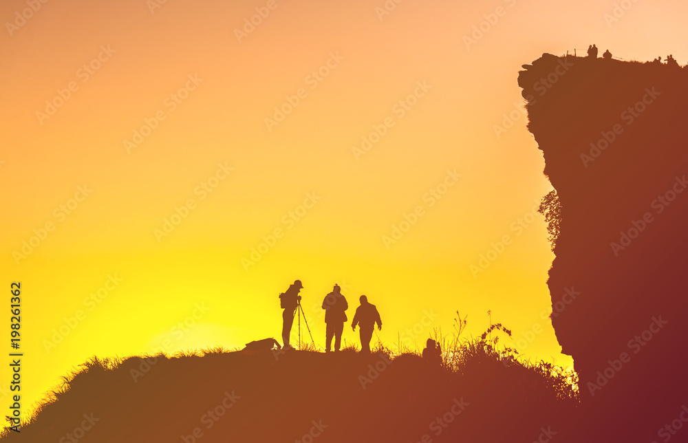 Silhouettes of people standing on peak of sandstone rock in Phu Chi Fa Nation Park and watching over misty and foggy morning . Chiang Rai in Thailand.