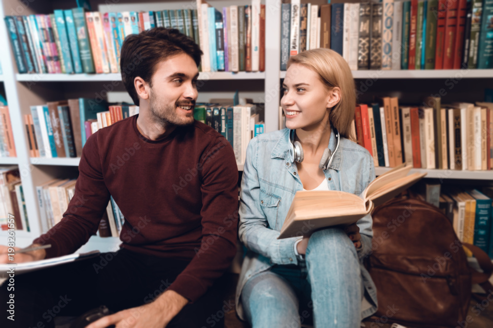 White guy and girl near bookshelf in library. Students are reading books. White guy and girl near bookshelf in library. Students are reading books.