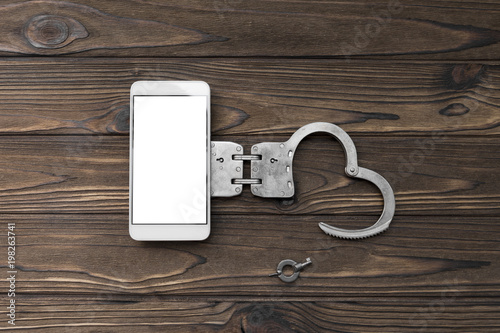 Wallpaper Mural smartphone with white screen, handcuffs on a wooden background. dependence on the Internet, mobile communications. Torontodigital.ca