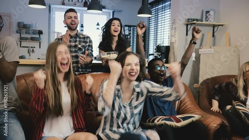 Multi-ethnic football fans celebrate winning. Slow motion 4K. Supporters go mad watching sports game on TV. Emotion.