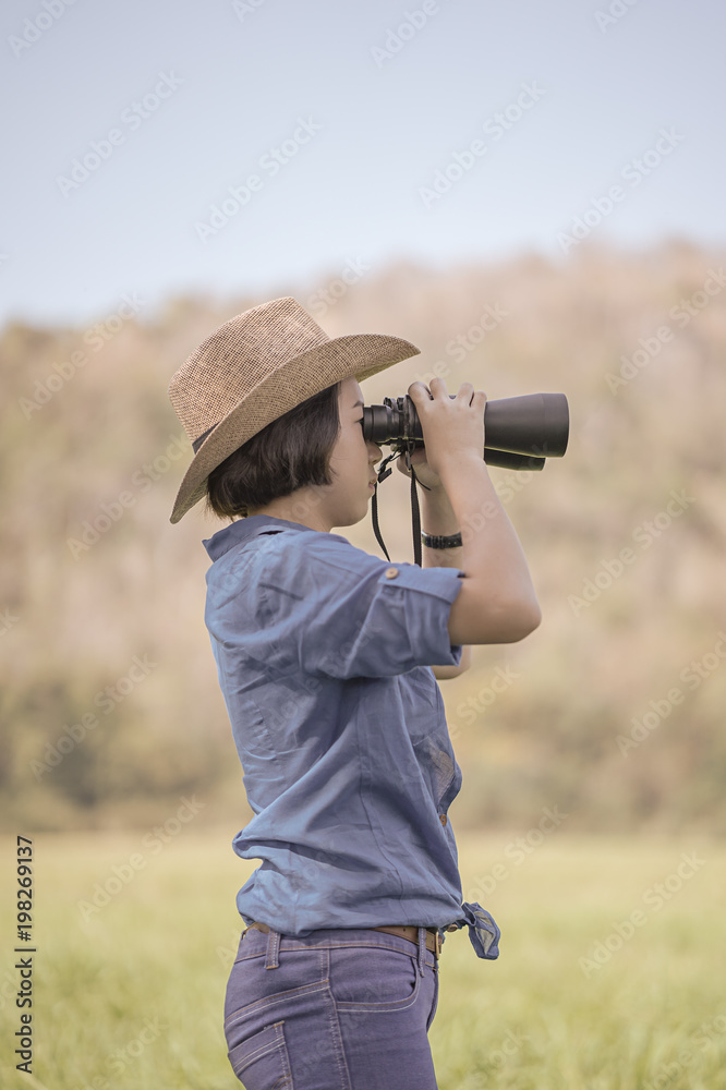 Woman wear hat and hold binocular in grass field Woman wear hat and hold binocular in grass field